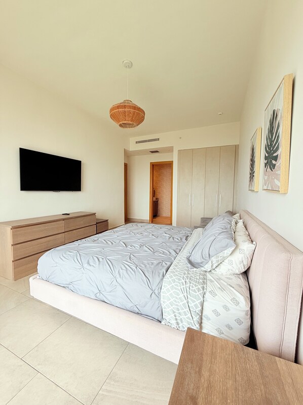 A modern bedroom with a large bed, a TV mounted on the wall, and a wardrobe.
