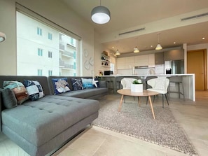 A modern living room with a grey sofa, a round coffee table, and a kitchen area in the background.
