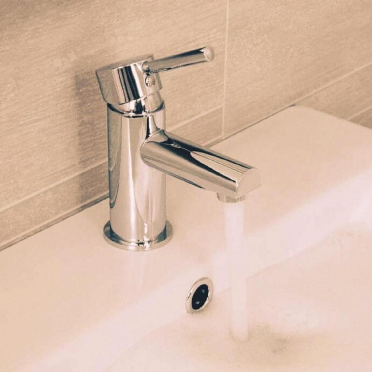 A chrome faucet with a single-handle design, positioned above a white sink with a drain.
