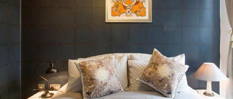A bedroom with a bed, two decorative pillows, a framed artwork above the bed, a bedside lamp, and a nightstand.