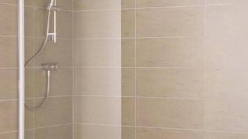 Un espace douche d’angle avec une baignoire, une douchette à main et un robinet mural.