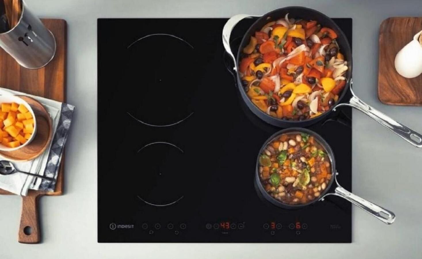 A kitchen with an induction cooktop, a pot with vegetables, and a bowl of food on a wooden board.