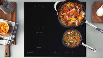 A kitchen with an induction cooktop, a pot with vegetables, and a bowl of food on a wooden board.
