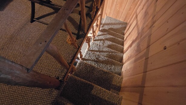 Eine Holztreppe mit Geländer, Teppichstufen und einer Holzzieldecke.