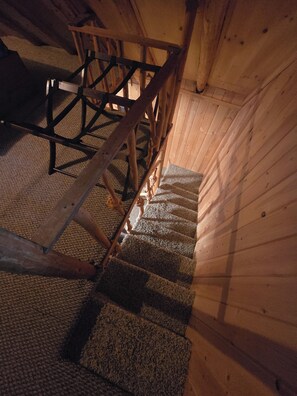 A wooden staircase with a handrail, carpeted steps, and a wooden ceiling.