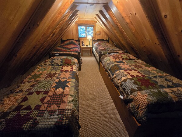 A narrow attic bedroom with two beds, a window, and a wooden ceiling.