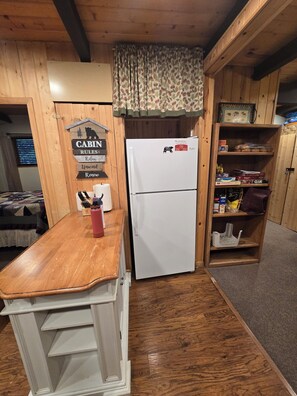 Une cuisine de style rustique, avec un plan de travail en bois, un réfrigérateur blanc et un panneau décoratif placé au-dessus du réfrigérateur.