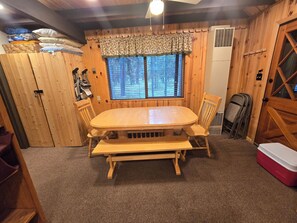 Un intérieur en bois comprenant une table à manger, des chaises, un banc, une fenêtre avec des stores, un ventilateur de plafond et un réfrigérateur rouge.