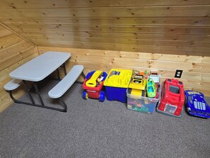 L’intérieur d’une cabane en bois, avec une table de pique-nique et divers véhicules jouets.