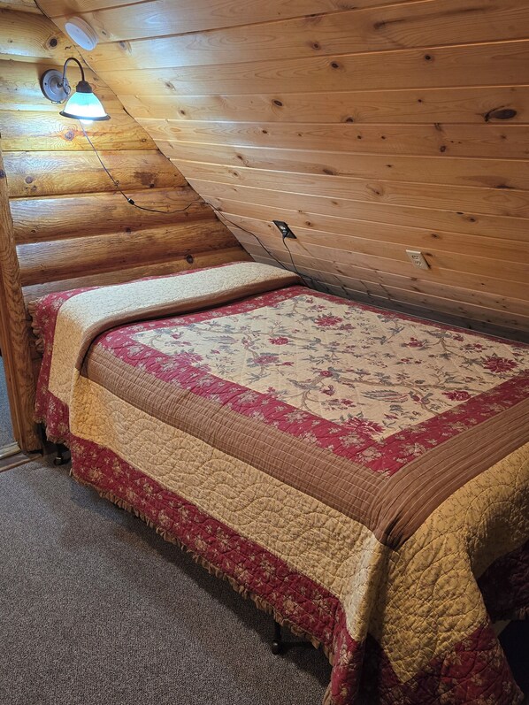 L’intérieur d’une cabane en bois, avec un lit, une lampe fixée au mur et une prise de courant.