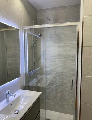Ein modernes Badezimmer mit einer gläsernen Duschkabine, einem weißen Waschbecken und einem großen Spiegel.