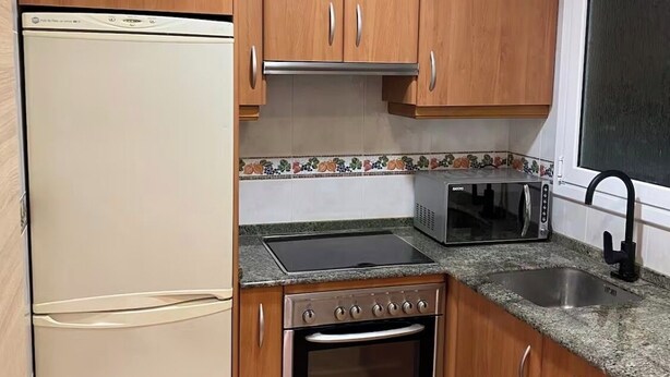 A compact kitchen with wooden cabinets, a built-in oven, a microwave, and a refrigerator. - 
Central 2-Bedroom Apartment in Barcelona. (Barcelona)