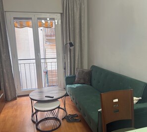 Ein Wohnzimmer mit einem grünen Sofa, einem runden Tisch und einem Paar Hausschuhe.