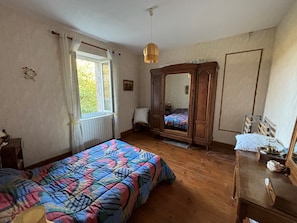 A bedroom with a bed, a wooden wardrobe, a bedside table, a window with curtains, and a hanging light fixture. - Country House for Rent (Lestrade-et-Thouels)