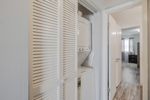 A laundry room with a washer and dryer, a door leading to a bathroom, and a hallway with a tiled floor. - Turtle House - Quiet 2BR 2BA - Seconds from beach, short walk to Pier Park. (Panama City Beach)