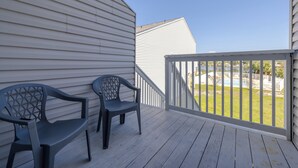 Eine Holzterrasse mit zwei Stühlen und einem Geländer, das auf eine Rasenfläche blickt.