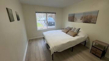A bedroom with a bed, a nightstand, and a window with a view of the outside.