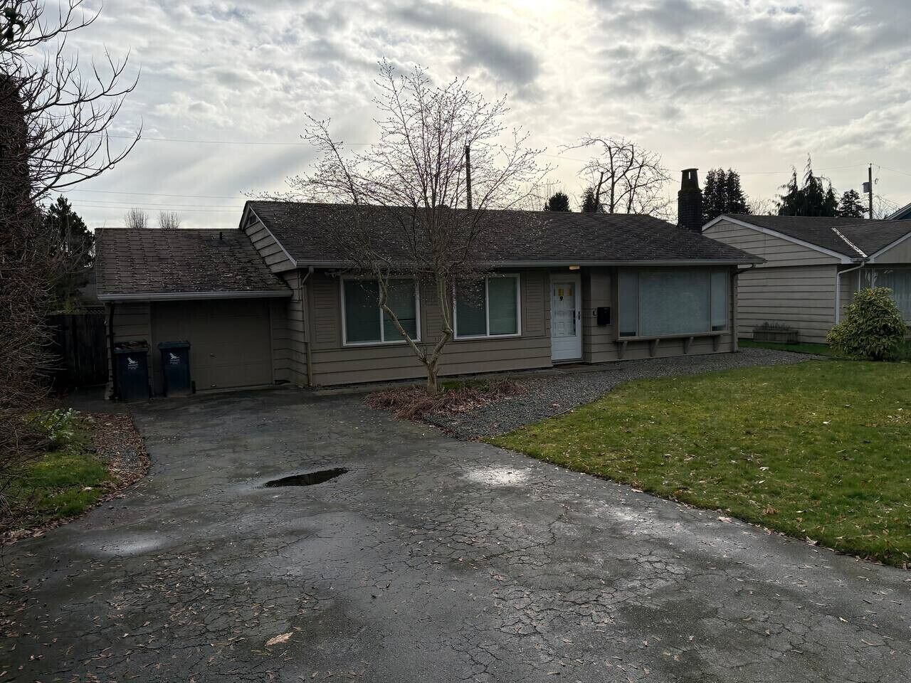 A residential building with a garage, a small lawn, and a tree in front.