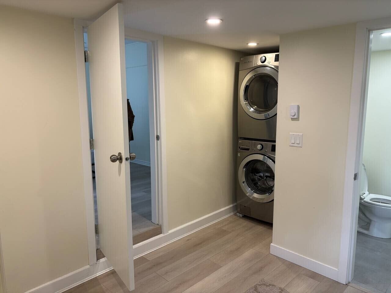A laundry room with a washing machine and dryer, a door leading to another room, and a light switch on the wall.