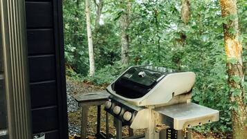 Ein Grillplatz im Freien mit Gasflasche und tragbarem Tisch, umgeben von einem Waldgebiet.