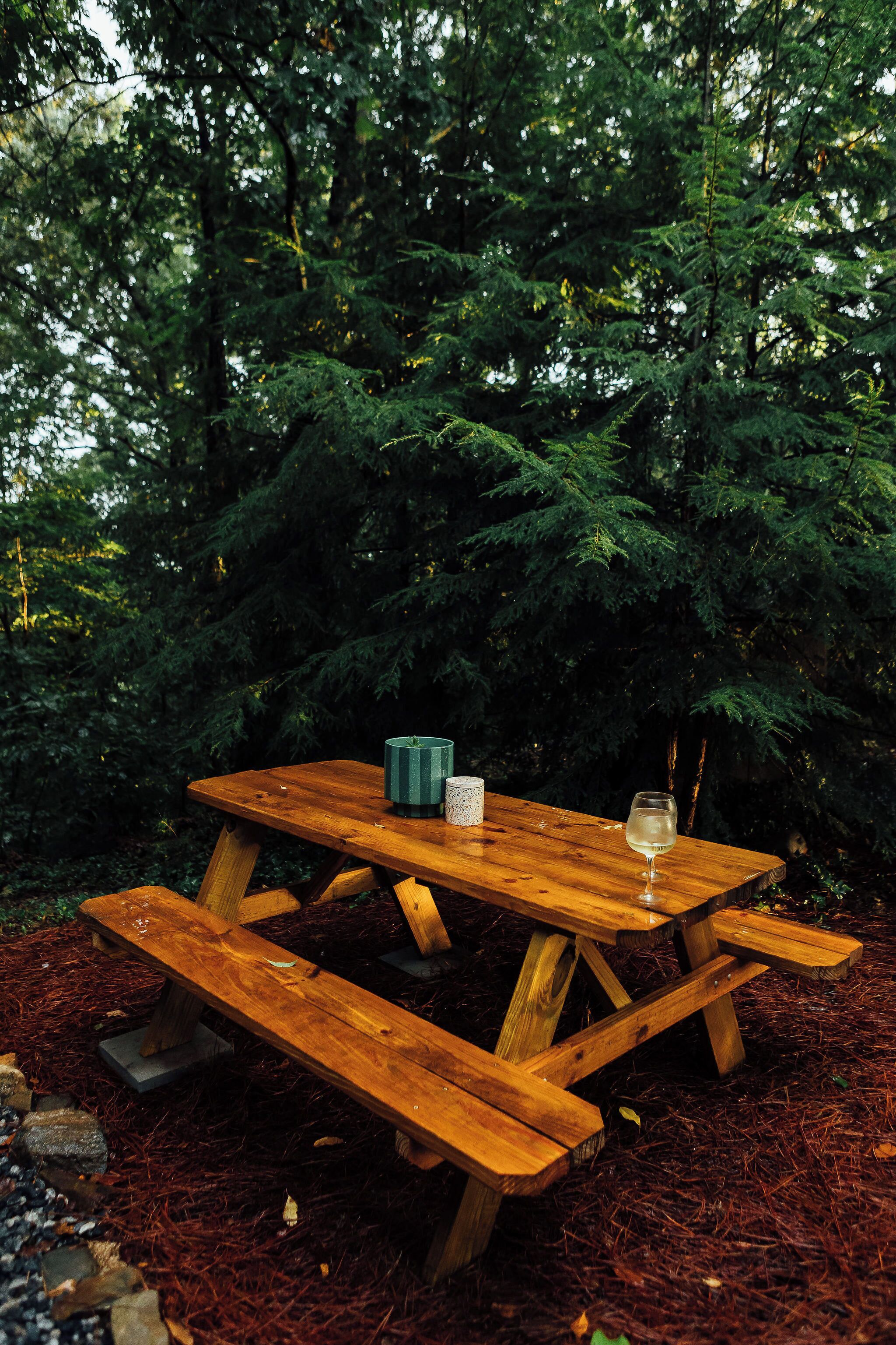 A wooden picnic table with benches, a green mug, and a glass of water.