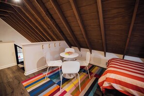 A small, cozy room with a sloped ceiling, a white round table with chairs, a colorful striped rug, and a bed with a striped blanket. - Azalea Ridge Retreat - Cozy family cabin near Dahlonega (Dahlonega)