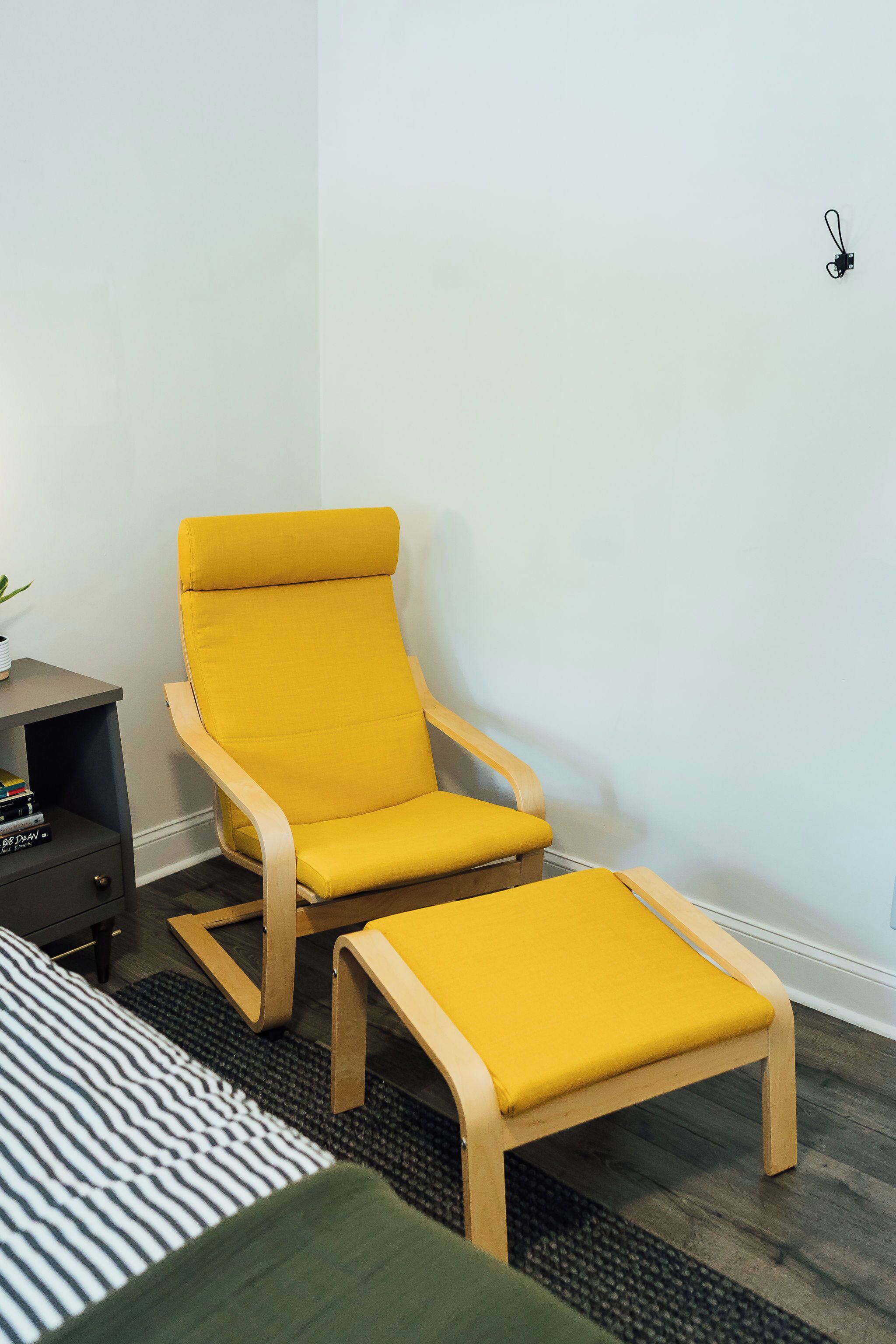 A yellow armchair with a matching ottoman in a room with a dark wooden floor and a striped rug.