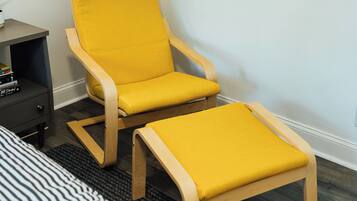 A yellow armchair with a matching ottoman in a room with a dark wooden floor and a striped rug.