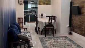A living room with a sofa, a dining table with chairs, a ceiling fan, and a TV mounted on the wall.