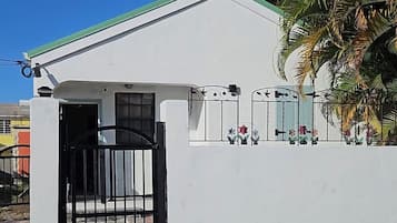 Un edificio blanco con entrada protegida por una reja, un pequeño porche y una palmera al fondo.