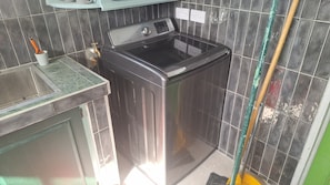 A compact laundry area with a washing machine, a sink, and a mop leaning against the wall.