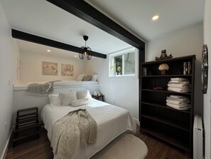 A bedroom with a bed, a nightstand, a bookshelf, and a window.