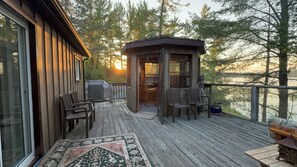 A wooden deck with outdoor seating and a covered area, overlooking a forested area.
