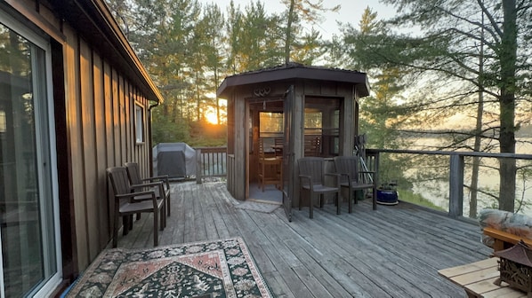 A wooden deck with outdoor seating and a covered area, overlooking a forested area.