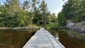 Puinen laituri, joka ulottuu tyynen vesialueen päälle, ja jota ympäröi tiheä metsä sekä pieni mökki.
