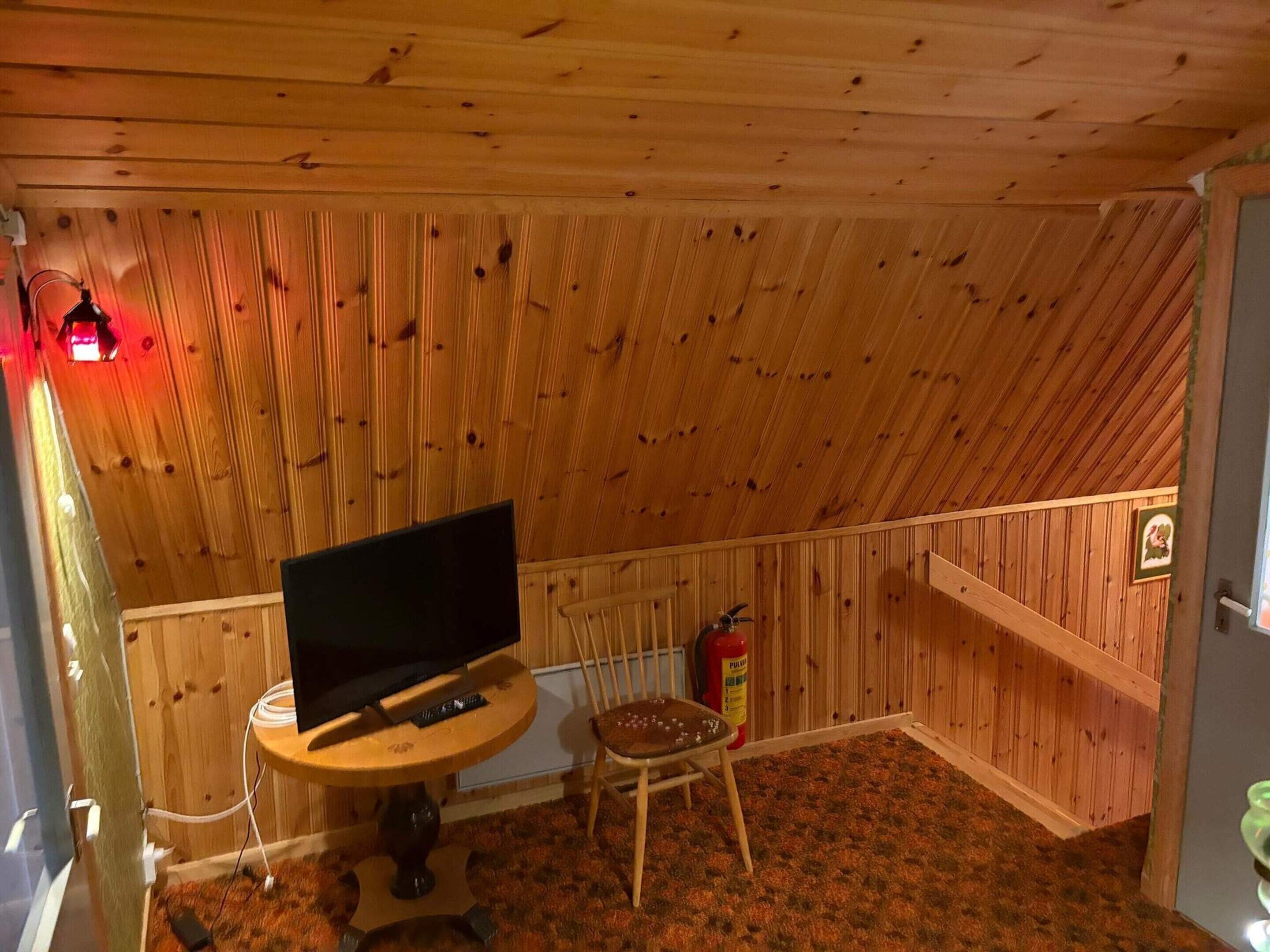 A wooden-paneled room with a television on a small table, a chair, and a fire extinguisher.