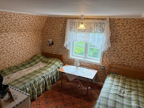 A room with two single beds, a small table with a lamp, a window with curtains, and a patterned wallpaper. - 4 Person Holiday Home in Hassela (Hassela)