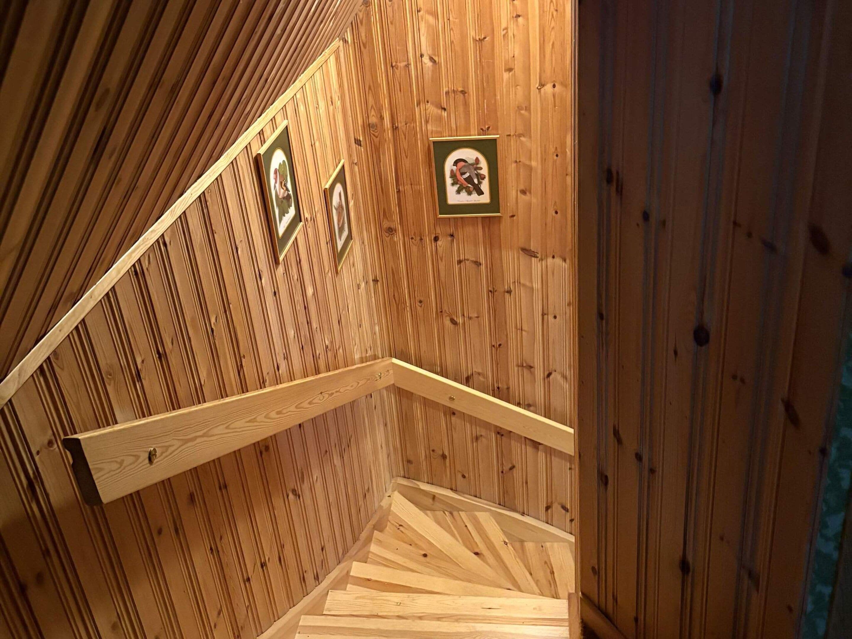 Un escalier en bois avec une rampe, des murs en bois et des tableaux encadrés.