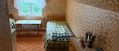Un dormitorio con una cama, un aparador, una mesita de noche con lámpara y una ventana con cortinas.
