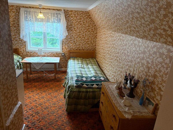 A bedroom with a bed, a dresser, a table with a lamp, and a window with curtains.