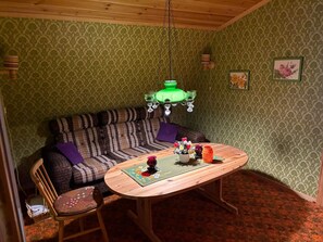 A room with a patterned green wallpaper, a striped sofa, a wooden table with a placemat, and a hanging green chandelier. - 4 Person Holiday Home in Hassela (Hassela)