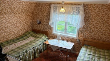 A room with two single beds, a small table with a lamp, and a window with curtains.