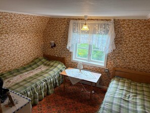 Een kamer met twee eenpersoonsbedden, een tafeltje met een lamp en een raam met gordijnen.