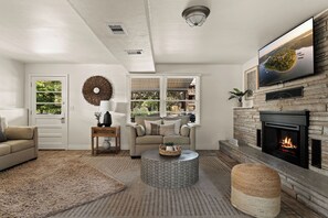 A living room with a fireplace, a sofa, a coffee table, and a television mounted on the wall. - Magnolia House Retreat at Stillwaters Resort (Branson)