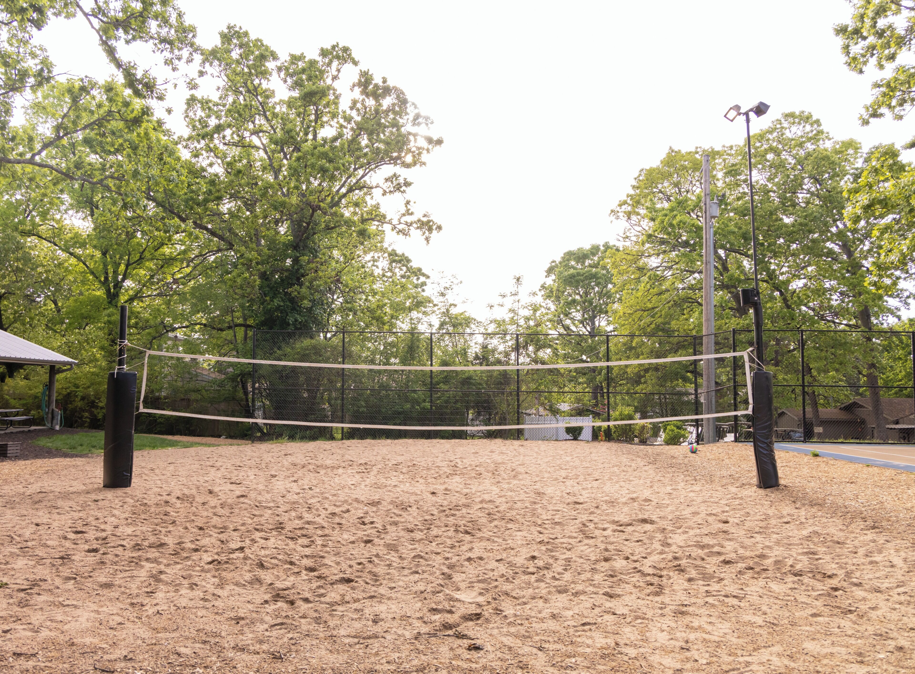 Un terrain de volleyball de sable avec un filet, entouré d’arbres et d’une clôture.