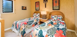 A room with two beds, a nightstand, a lamp, and tropical-themed wall art.