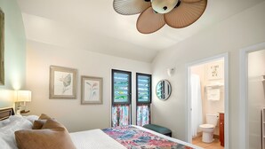 A hotel room with a bed, a large window with curtains, a ceiling fan, and artwork on the walls. - Breezy 4BR, 2 Condos for 12 at Kaha Lani, Lihue! (Lihue)