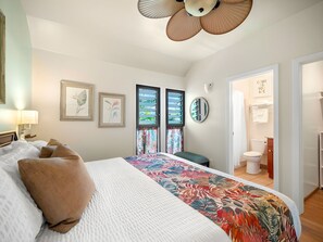 A hotel room with a bed, a large window with curtains, a ceiling fan, and artwork on the walls. - Breezy 4BR, 2 Condos for 12 at Kaha Lani, Lihue! (Lihue)