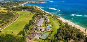 An aerial view of a coastal property with a tennis court, a swimming pool, and a beach.