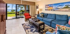 A living room with a sofa, a red chair, a coffee table, and a view of the ocean through a sliding glass door.